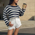 Woman wearing a striped long-sleeved cropped sweater in mercerised cotton, showcasing front and back wearable design.