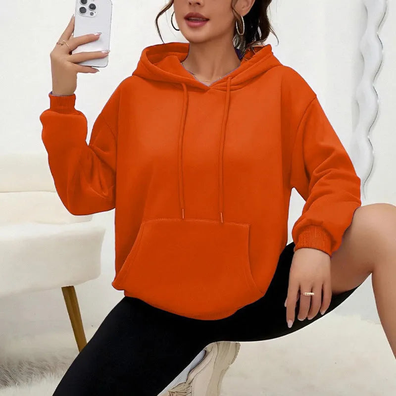 Woman wearing a loose-fitting black hooded sweatshirt with a front kangaroo pocket.