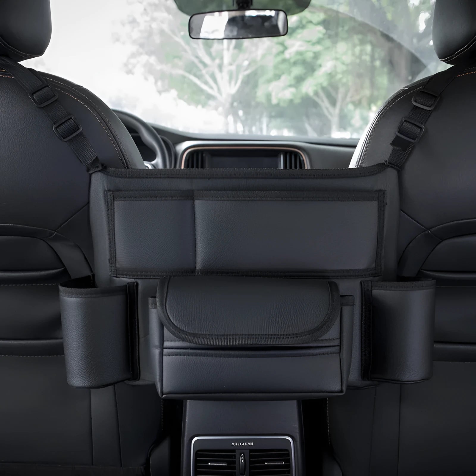 Black leather car interseat storage bag holding a tissue box, hanging between vehicle front seats.