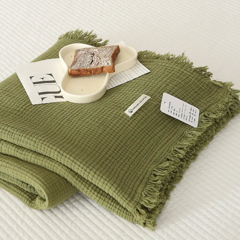 Cotton four-layer gauze blanket with tassel trim in various colours draped over a sofa.
