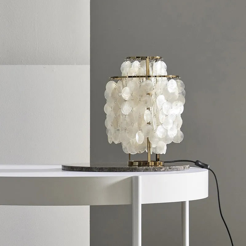 Creative modern shell-shaped table lamp in chrome or gold finish on a bedside table.