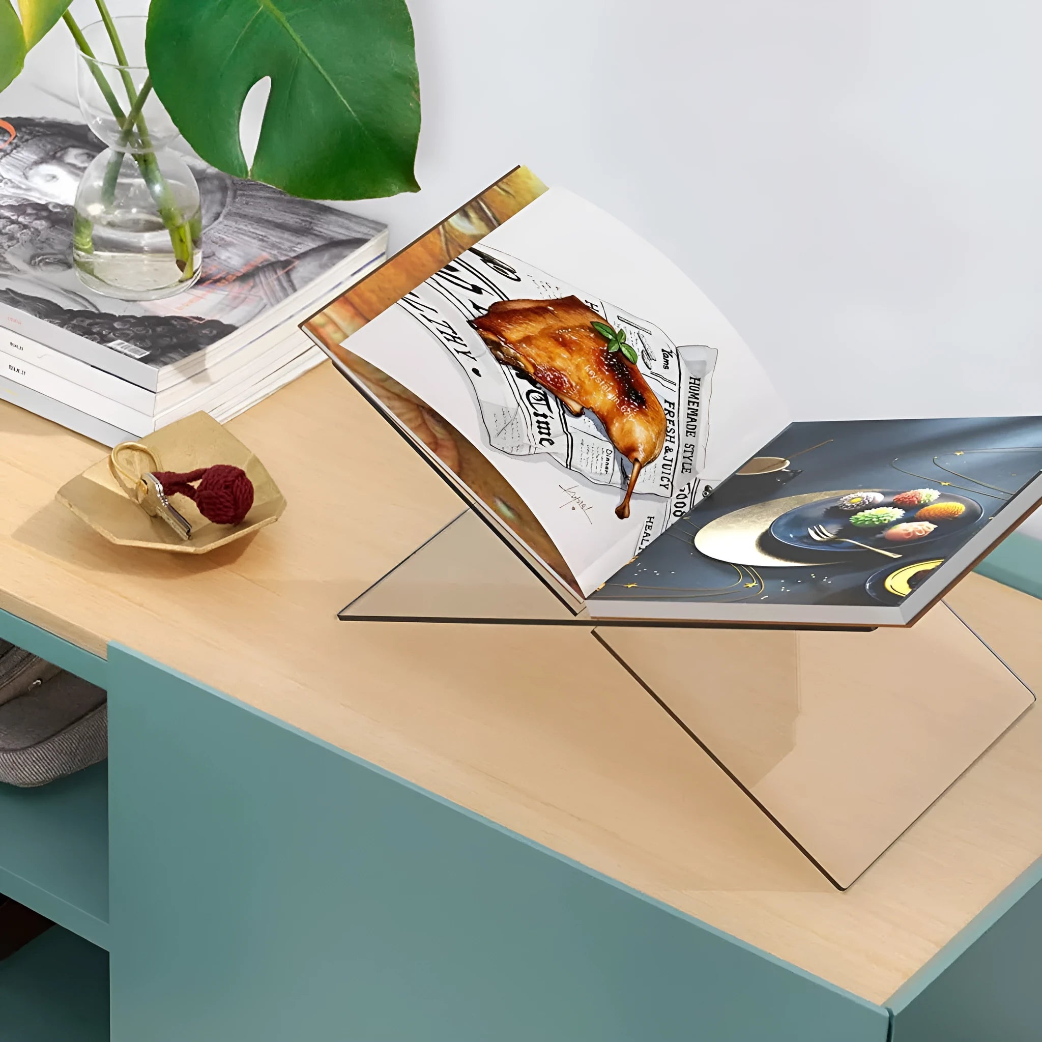 Clear acrylic X-shaped book display stand holding a hardback book on a wooden desk.