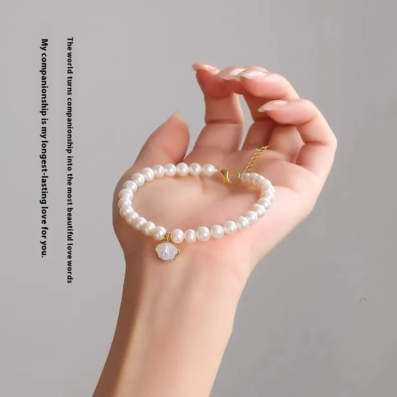 Women's freshwater pearl bracelet with fan-shaped charm on wrist, showing elastic and chain fastening options.