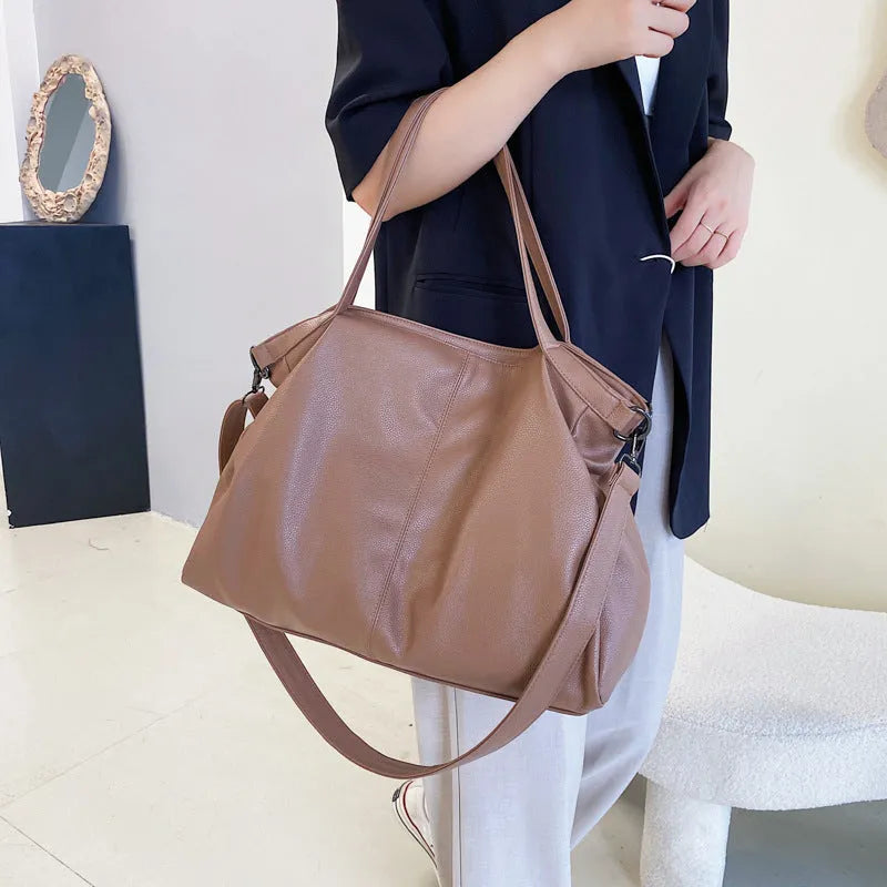 Large soft surface black messenger bag with soft handle and long shoulder strap on a table