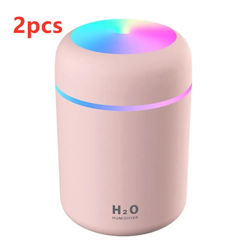 Pink USB desktop humidifier with LED lights and water tank on a wooden desk.