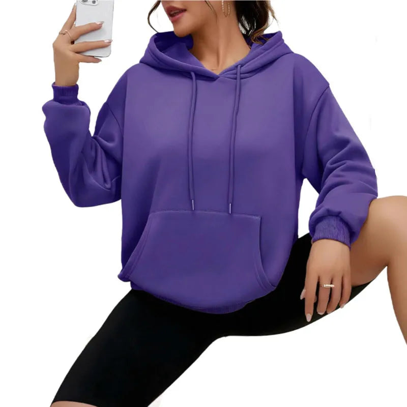 Woman wearing a loose-fitting black hooded sweatshirt with a front kangaroo pocket.