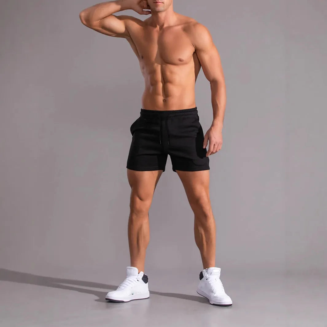 Three pairs of men's solid colour drawstring shorts in black, khaki and light brown laid flat