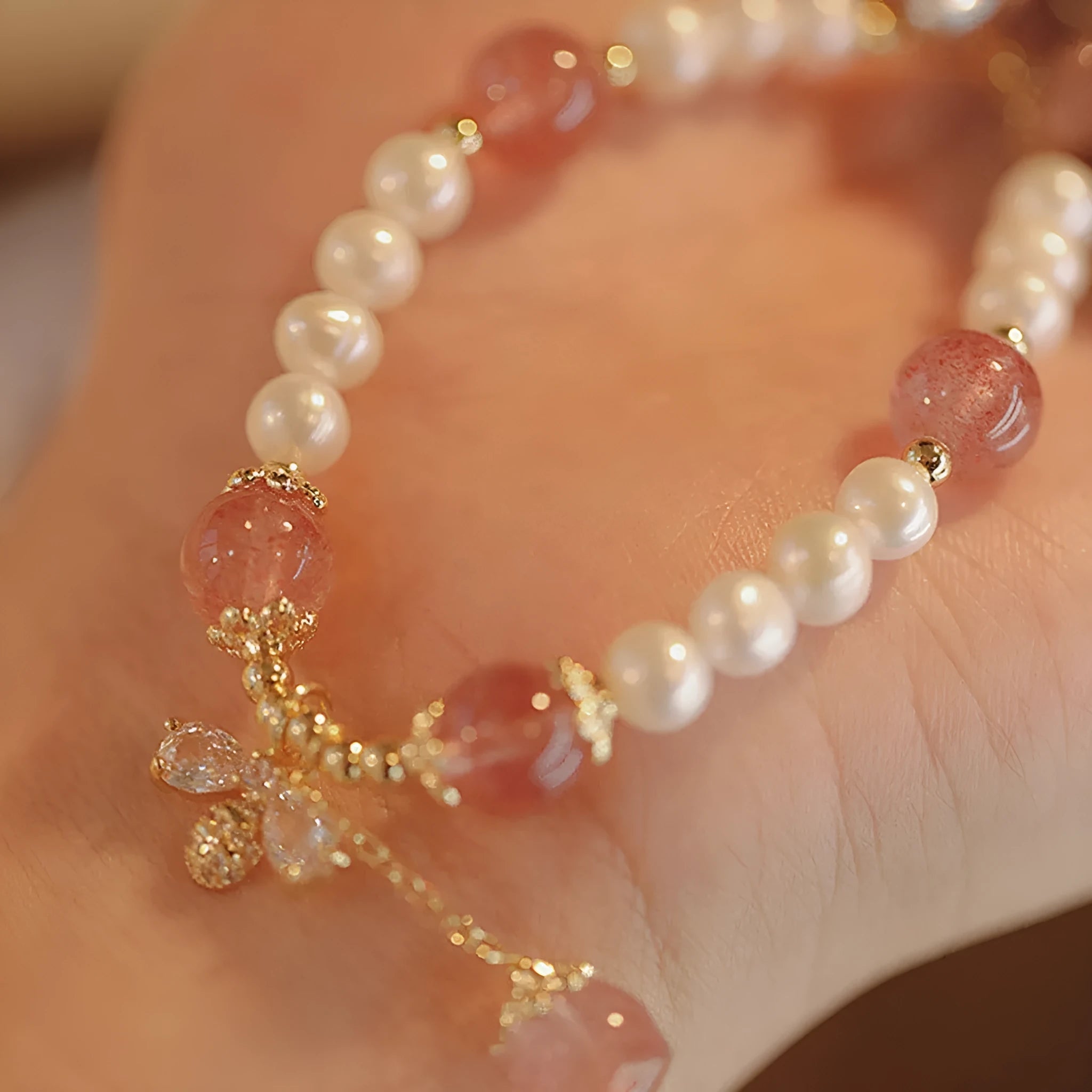 Women's strawberry quartz crystal bracelet with pearls and bow charm on wrist
