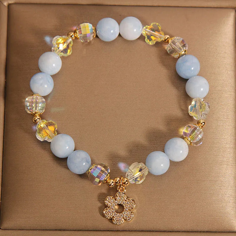 Women's bracelet with aquamarine crystal clover charm and white pearl details on a light background.