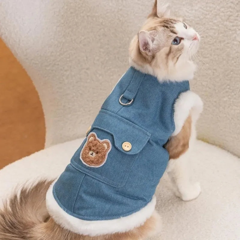 Denim dog vest with white wool lining, embroidered teddy bear patches, wooden buttons, and metal D-ring on blue background
