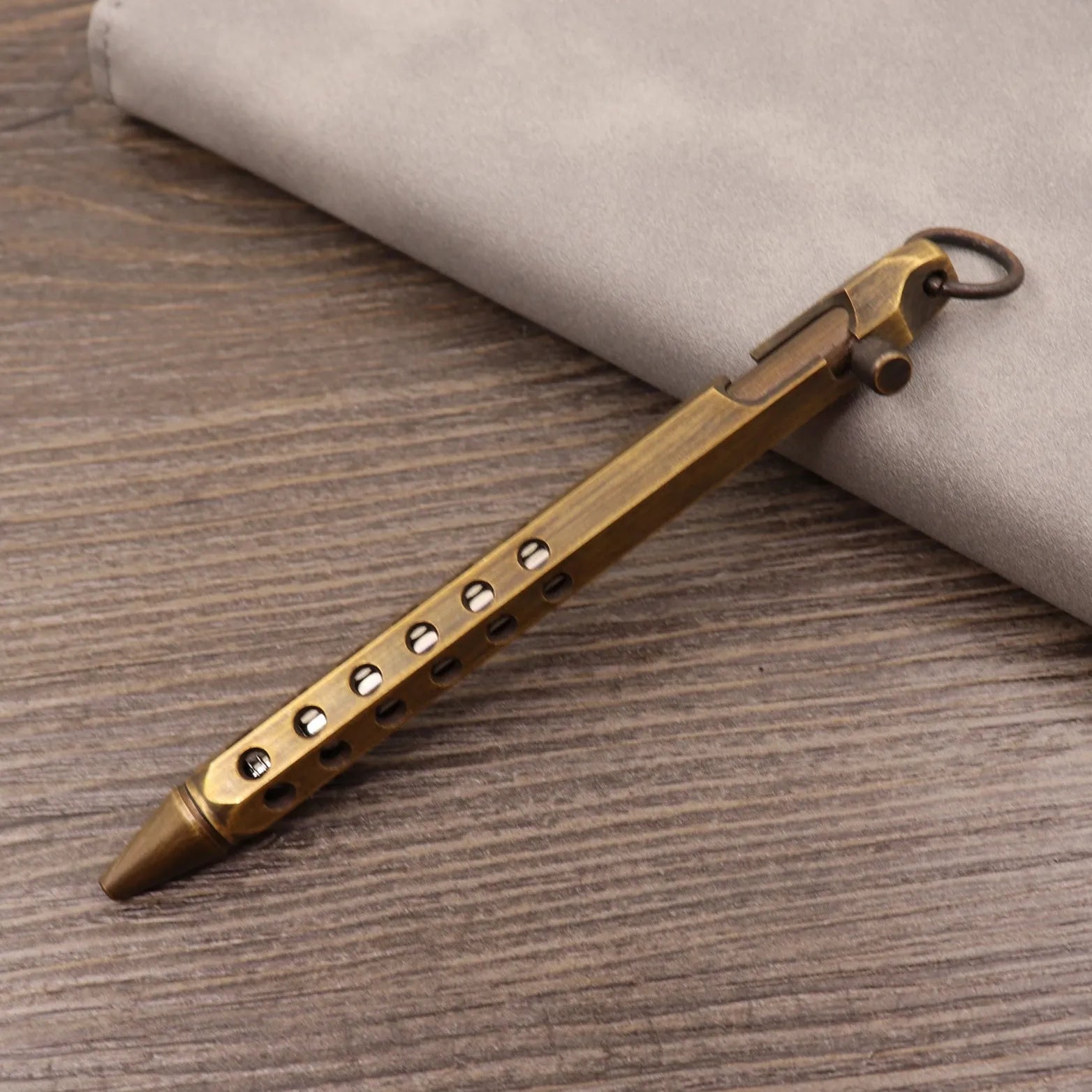 Close-up of a solid brass bolt action tactical pen with a press mechanism on a dark surface.