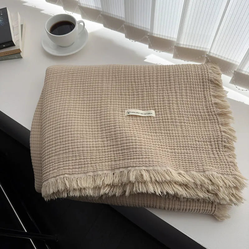 Cotton four-layer gauze blanket with tassel trim in various colours draped over a sofa.