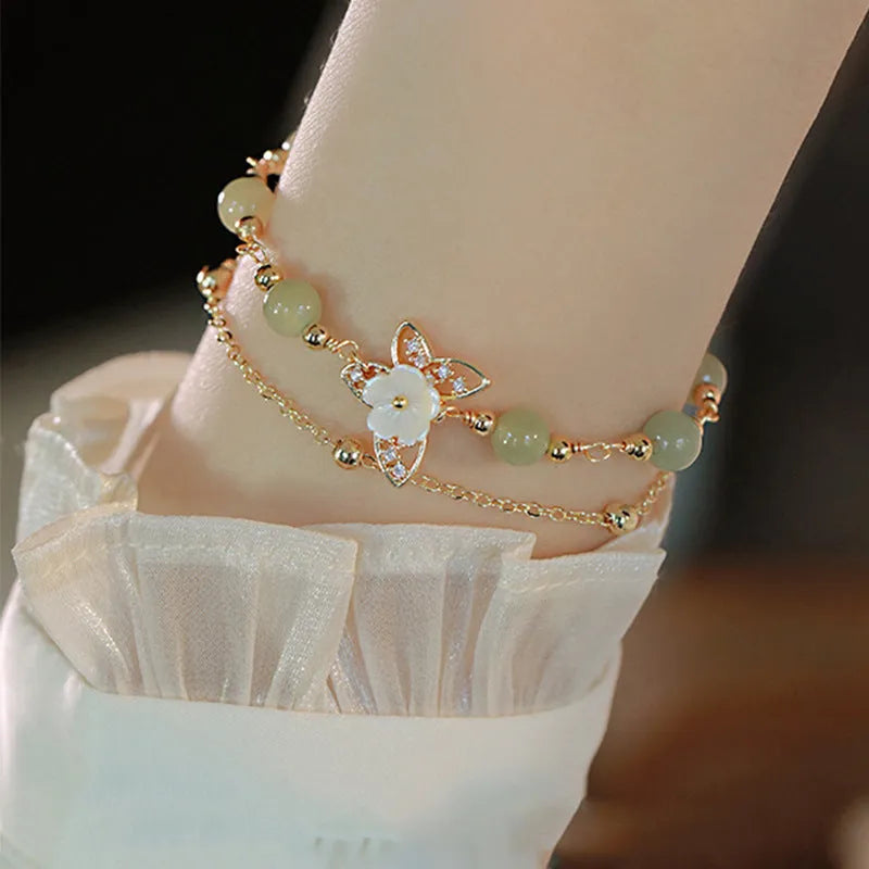 Yellow gold electroplated copper bracelet with a bells of Ireland butterfly, shell flowers, and Hetian jade accents.