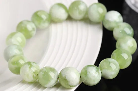Green milk-in-water Xiuyan jade polished bracelet with geometric beads on a neutral background