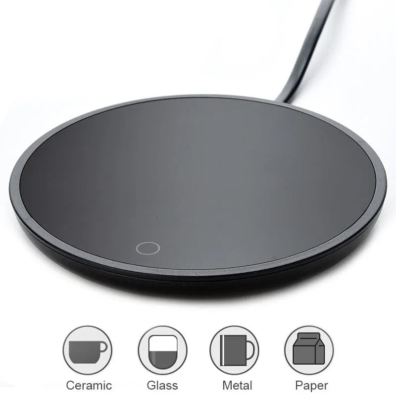Black circular coffee mug warmer with a tempered glass surface on a desk.