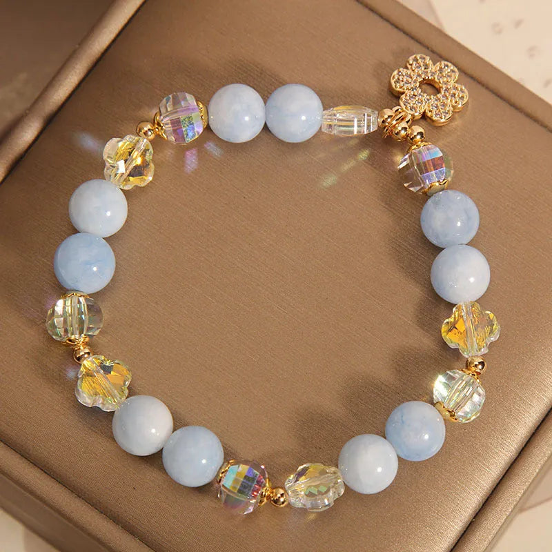 Women's bracelet with aquamarine crystal clover charm and white pearl details on a light background.