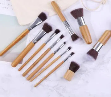 11 bamboo handle makeup brushes arranged on linen bag, including foundation blush and eye shadow brushes