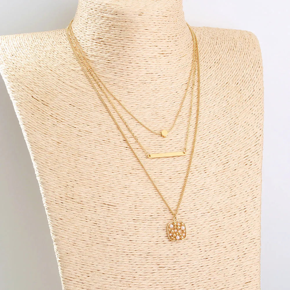 Gold multi-layer necklace with geometric pineapple pendant on a neutral background