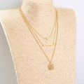 Gold multi-layer necklace with geometric pineapple pendant on a neutral background