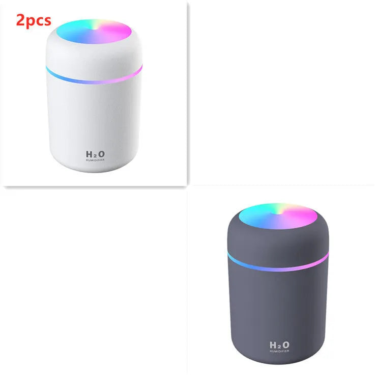Pink USB desktop humidifier with LED lights and water tank on a wooden desk.