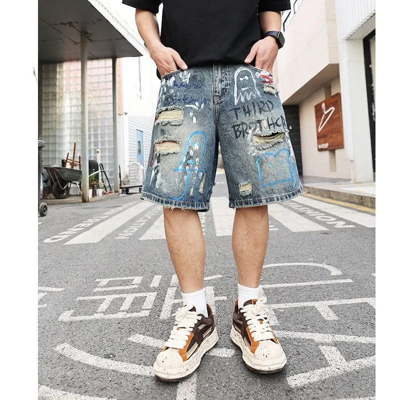 Blue men's denim shorts with ripped knees and graffiti detailing, showing straight leg cut and zipper fly.