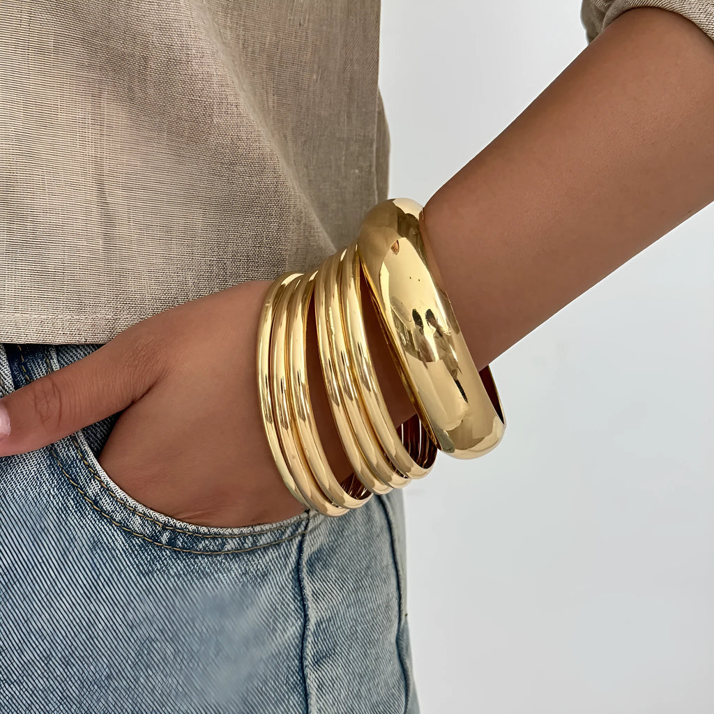 Exaggerated wide round glossy metal bracelet in gold tone on plain background
