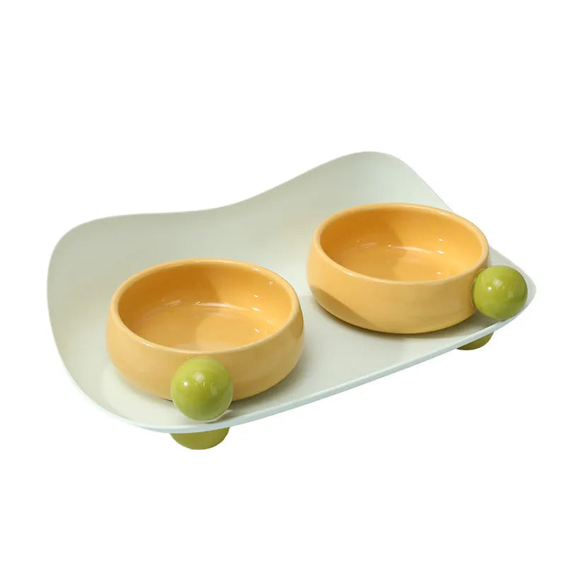 Raised ceramic double pet feeding bowl in pink, yellow, and pink yellow on a non-slip stand.