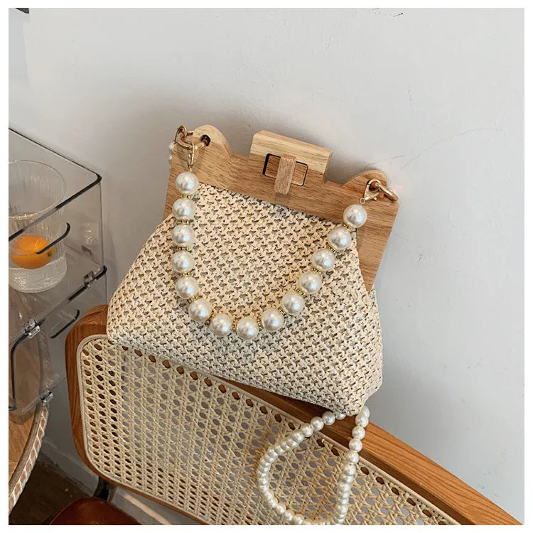 Women's woven straw shoulder bag with pearl chain strap in horizontal square shape showing sandwich pocket detail.