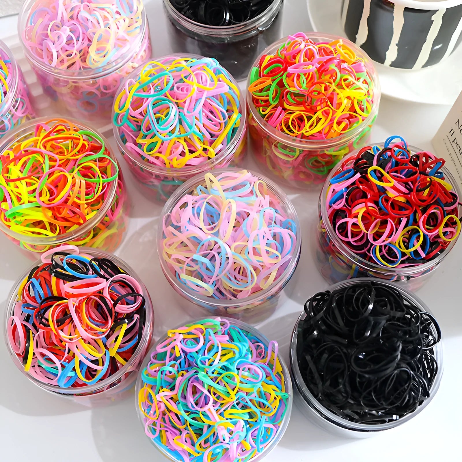 Open reusable container showing hundreds of thin, colourful TPU baby hair ties for toddlers.