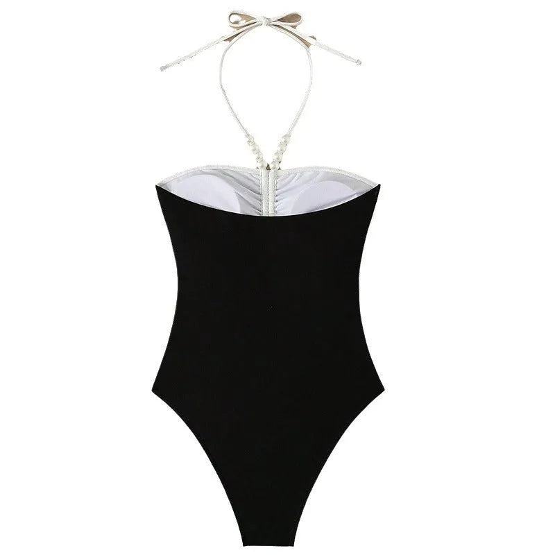 Black and white women's one-piece swimsuit with pearl spaghetti straps, shown on a model.