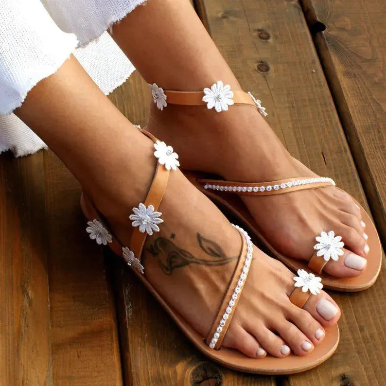 Brown women's Roman-style sandals with flat rubber sole and white floral decoration on the upper.