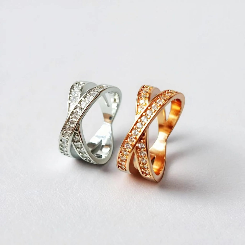 Simple metal cross ring with micro-inlaid zircon on a geometric band, shown in silver and rose gold finishes.