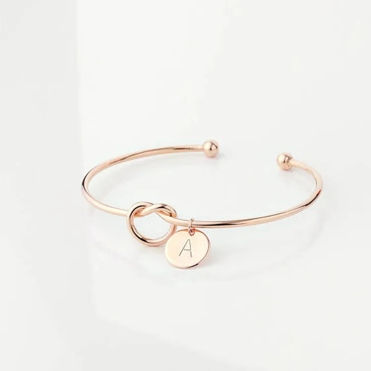 Personalised initial heart knot bracelet in gold finish with custom letter on a white background