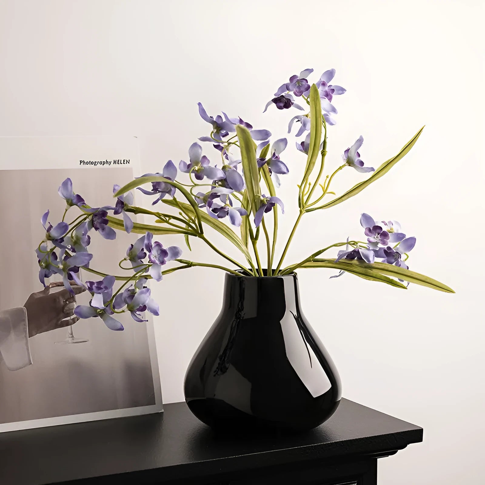 Black ceramic round belly vase with white artificial orchids on wooden table