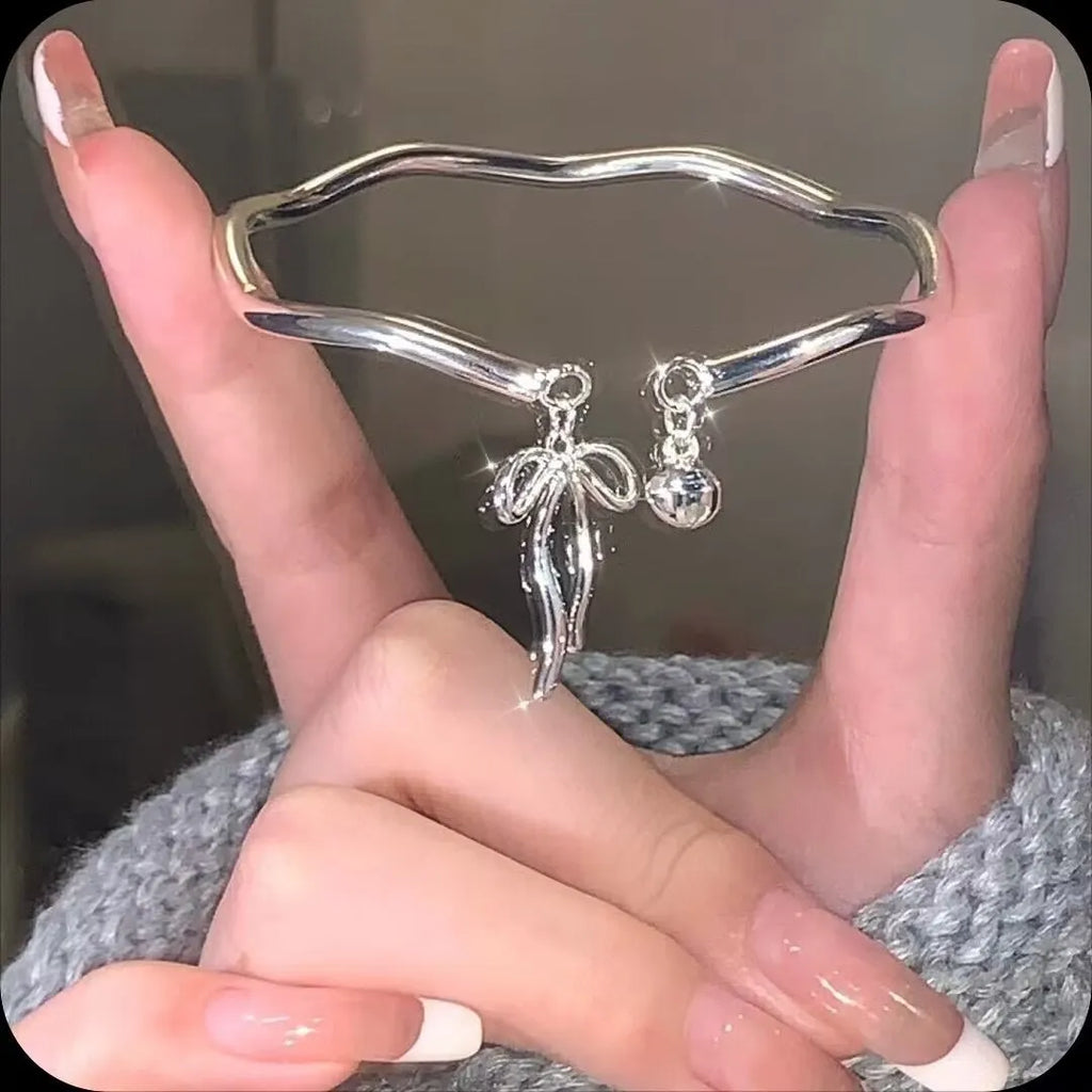 Silver tone adjustable bracelet with a bow charm on a white background.