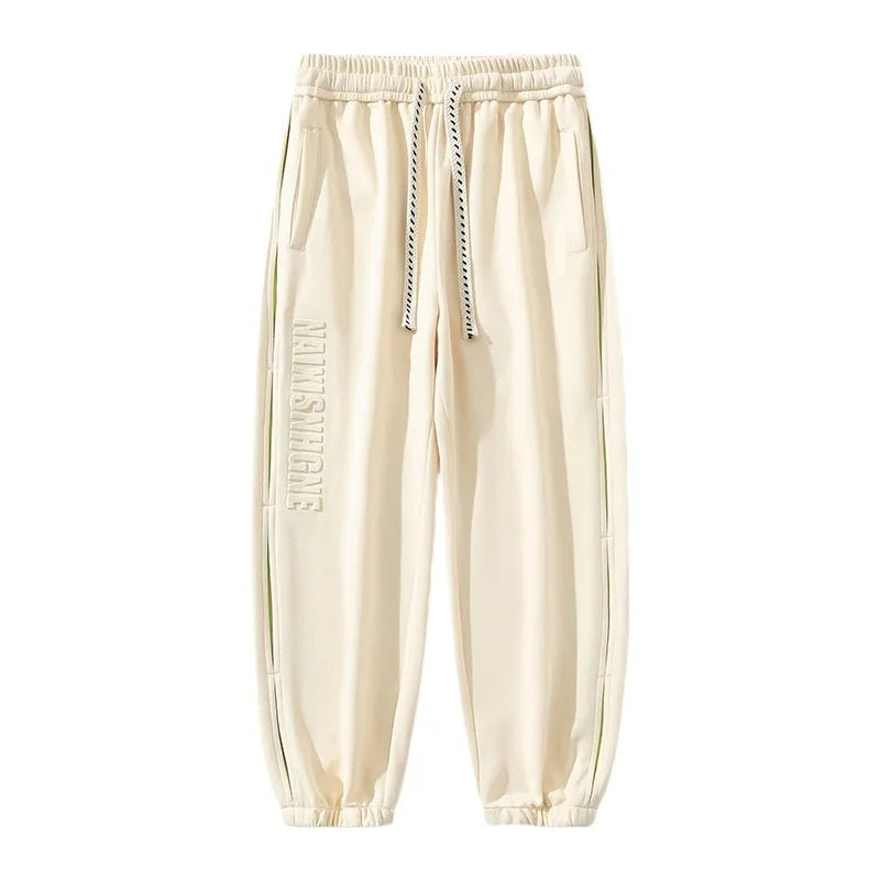 Men's loose black cotton trousers with white collage stitching print and banded ankle cuffs laid flat.