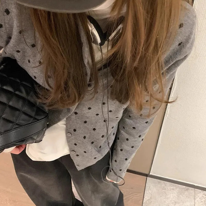 Women's grey dot pattern knitted cardigan with crochet flower details on sleeve.