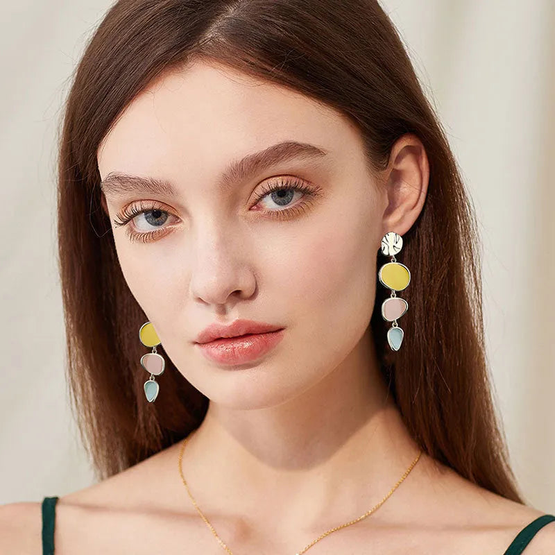 A pair of thin sterling silver stud earrings with Morandi-coloured wafer discs featuring an oil-drip texture.