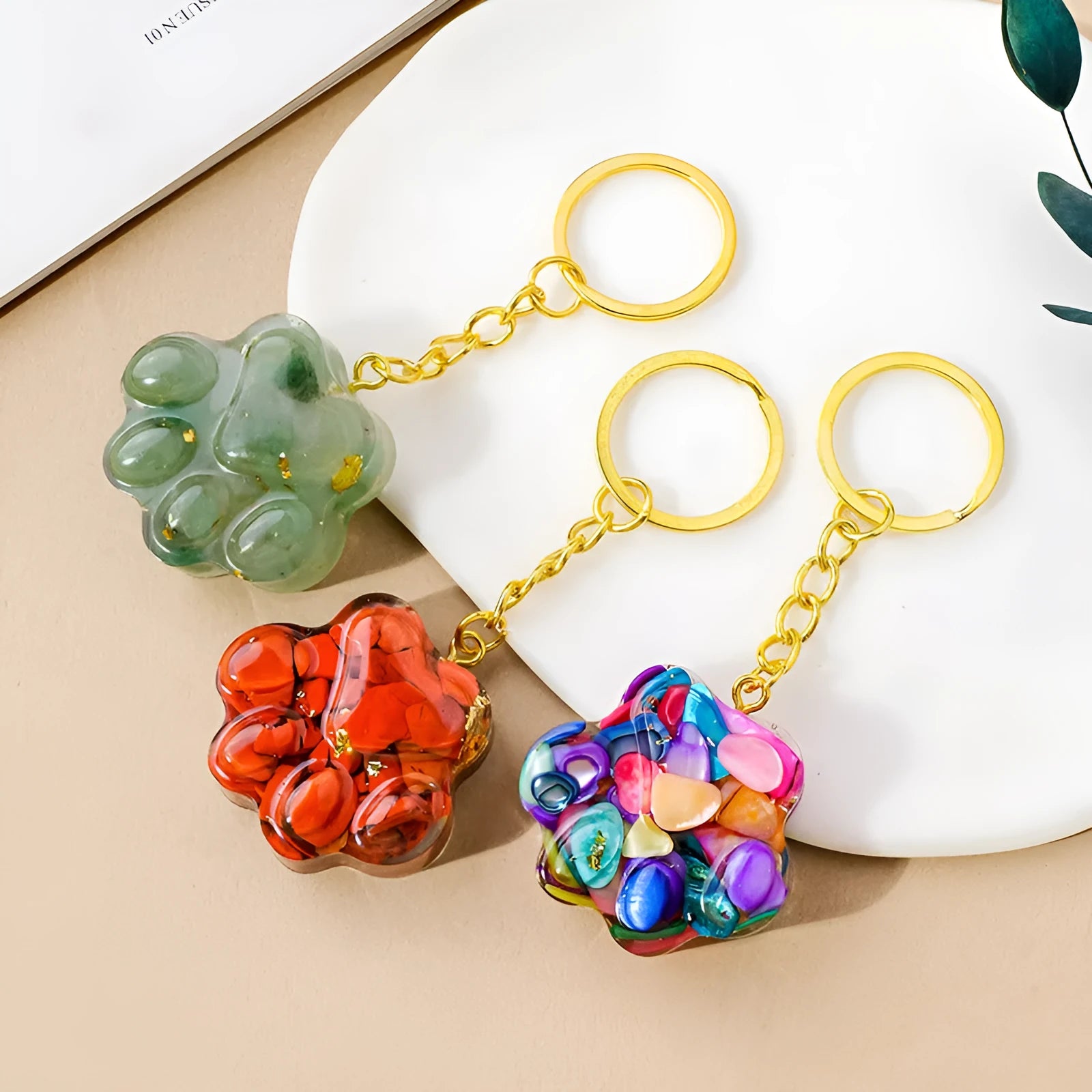 Small natural crystal cat's paw charm on a keyring, showing colour options including pink, red, blue, and purple gemstones.