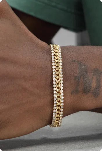 Gold coloured hip hop style tennis bracelet with stone inlay on a wrist.