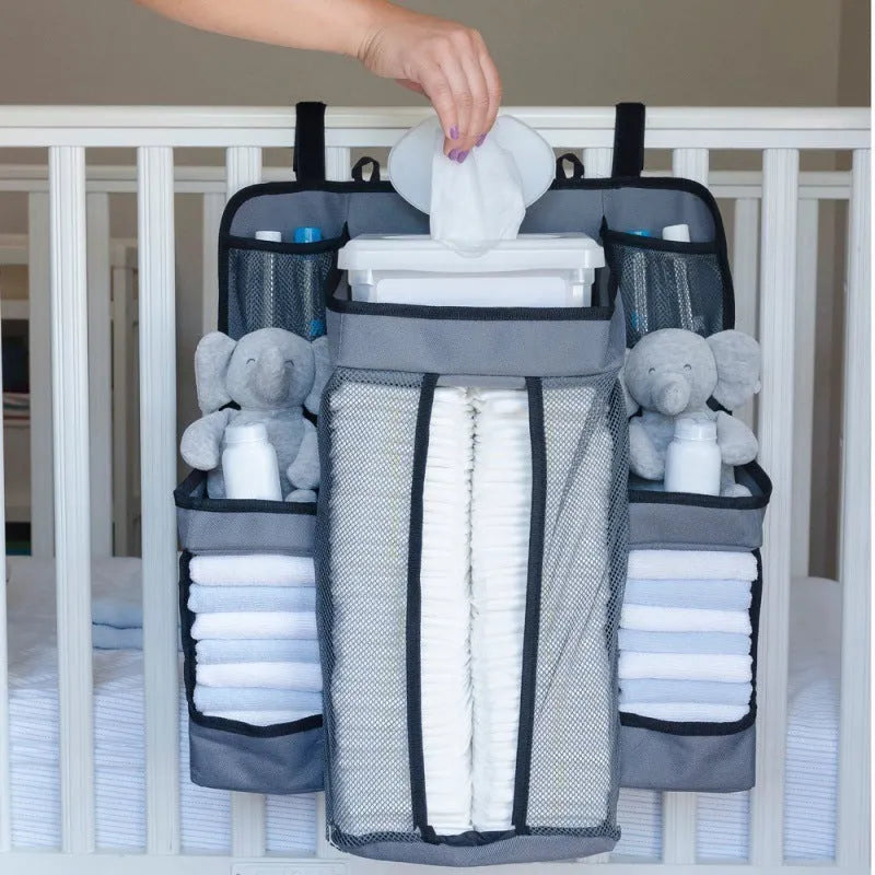 Gray baby diaper organizer hanging on a crib rail with compartments for nappies and wipes
