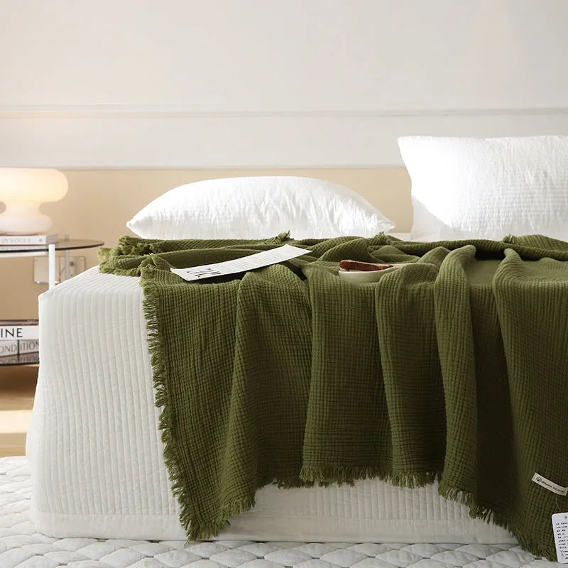 Cotton four-layer gauze blanket with tassel trim in various colours draped over a sofa.