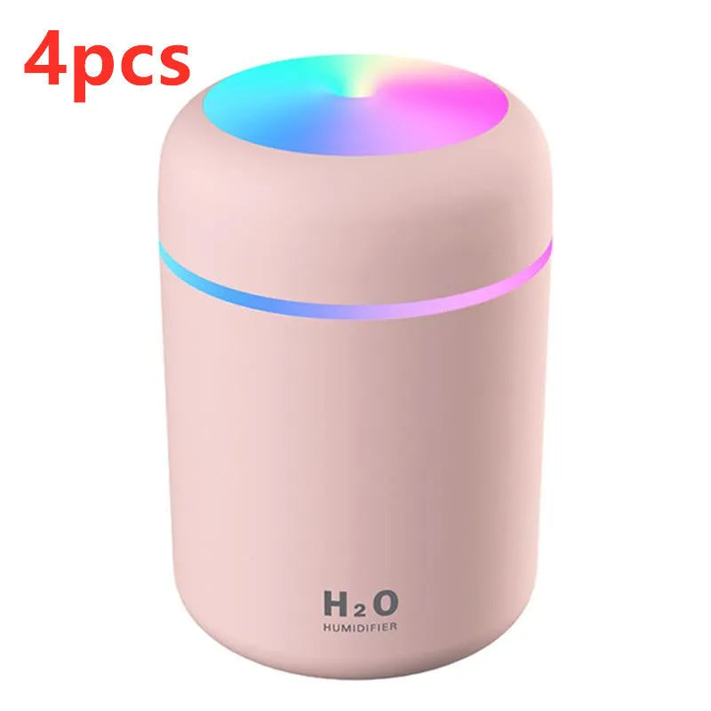 Pink USB desktop humidifier with LED lights and water tank on a wooden desk.