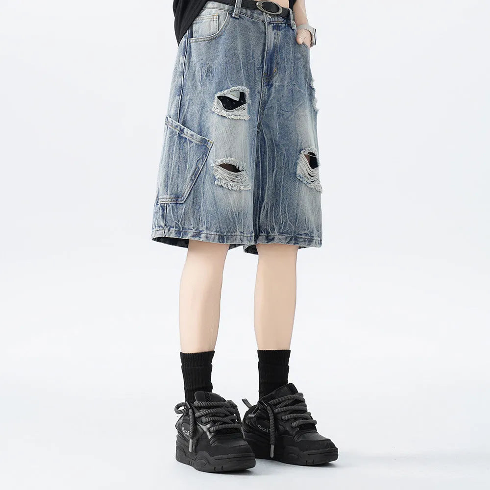 Man wearing loose blue ripped denim shorts with a vintage wash and distressed details.