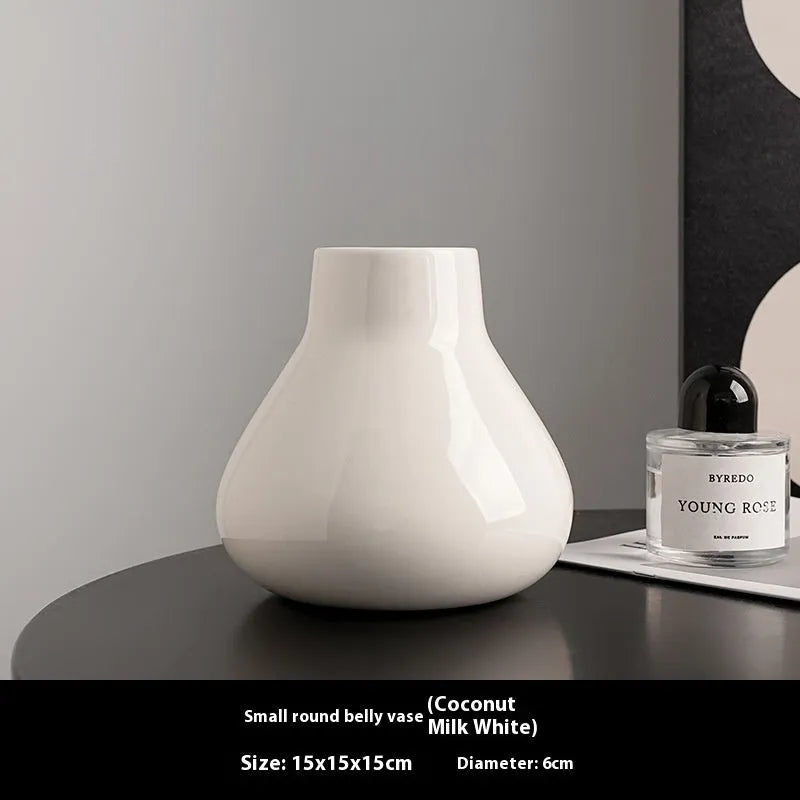 Black ceramic round belly vase with white artificial orchids on wooden table
