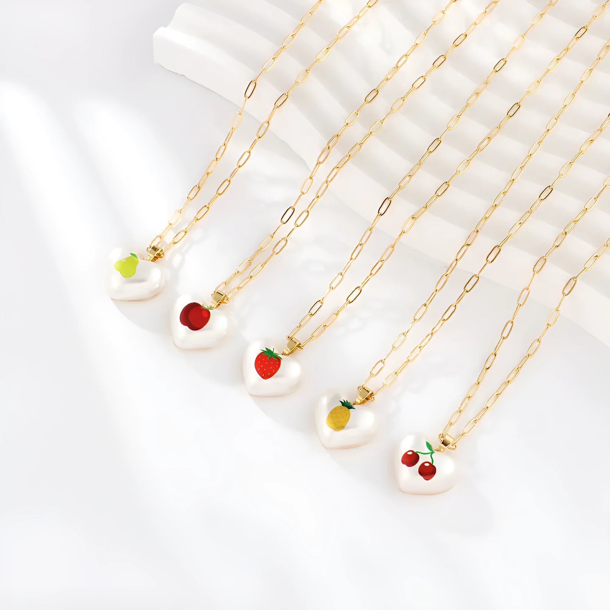 Geometric fruit charm necklace with an adjustable chain, shown in strawberry, pineapple, apple, pear, and cherry colour variants.