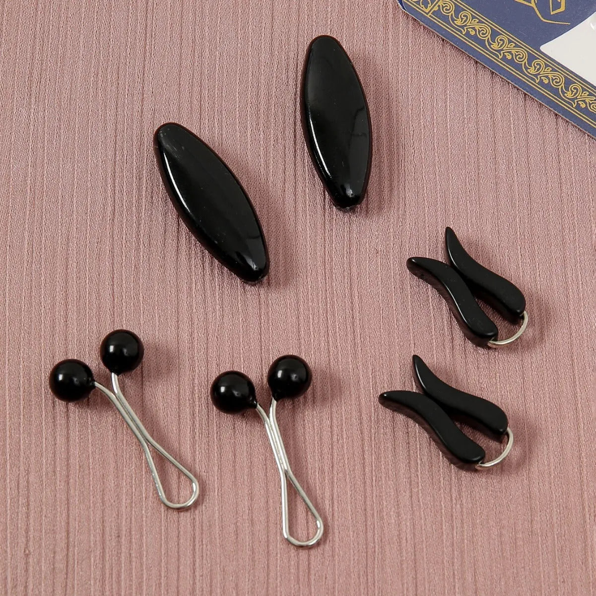 Plastic scarf clip with oval meander pattern and resin drip finish in five colours including black, gray, white, brown, and pink.