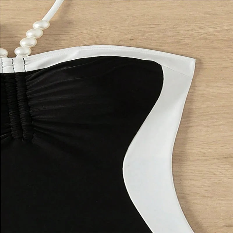 Black and white women's one-piece swimsuit with pearl spaghetti straps, shown on a model.