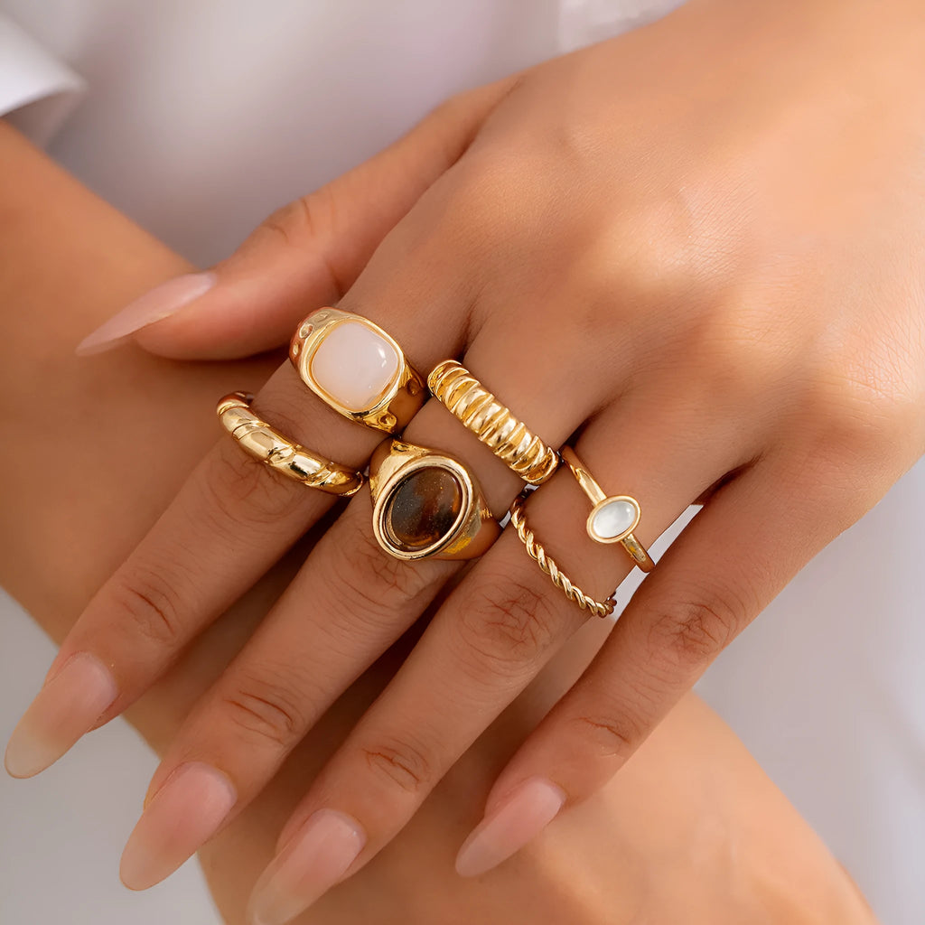 Six light gold alloy rings with geometric shapes and round elements arranged as a complete ring suit