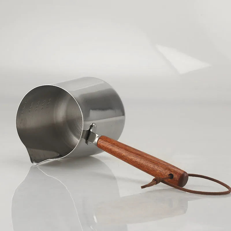 Stainless steel latte art milk cup with wooden handle and visible internal measurement scale.